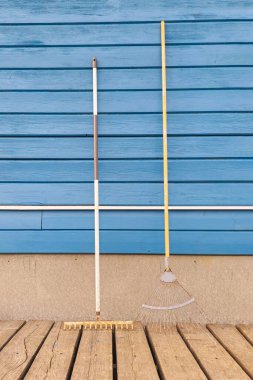 Mavi ahşap duvarın yanında gölgeli iki farklı bahçe tırmığı. Dikey görünüm. Boşluğu kopyala. 