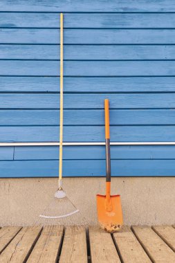 Bahçedeki tırmık ve turuncu maça, gölgeli mavi ahşap duvarın yanında. Dikey görünüm. Boşluğu kopyala. 