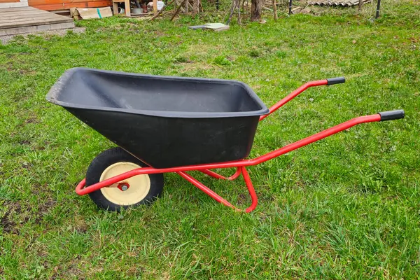 Yeni iki tekerlekli siyah metal el arabası, yeşil çimenli kırmızı çerçeveli..