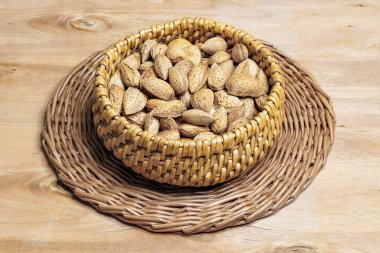 Tahta masadaki hasır bir kasede kabuklu badem. Üst görünüm, alanı kopyala.