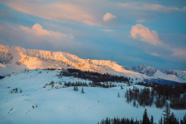 Alacakaranlıkta yüksek karlı dağların uzak manzarası. Kış Alacakaranlık Platosu. Dağlarda yakıcı bir günbatımı.