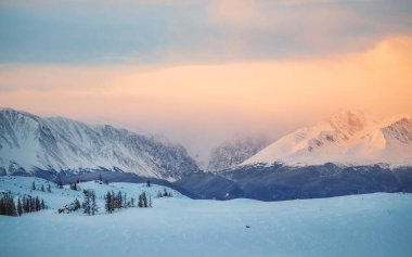 Kış zamanı. Güneşin doğuşunun panoramik görüntüsü ya da gün batımının karlı dağlardaki güneş ışığı sabah ya da akşam pembe ışık, bozkırın arka planındaki Altai dağları, dağlarda şafak vakti.