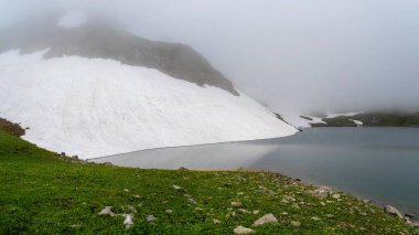 Alçak bulutlarda, sisli ve değişken havada buzul gölü. Buzul manzarası ve vadideki en güzel turkuaz buzul gölü. Panoramik görünüm.