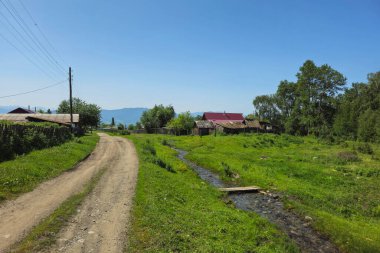 Tozlu kırsal bir yol. Eski ahşap bir ev, çitlerin arkasında bir arka bahçe. Güneşli bir yaz günü. Uzak Sibirya köyü Chendek, gerçek hayat. Ust-Koksinsky bölgesi. Rusya.