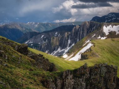 Rocky Dağı Vadisi. Terektinsky tepesi, Altai. Keskin uçurumları olan atmosferik dağ manzarası, yamaçlarda güneş ışığı ve dramatik karanlık bir gökyüzü..