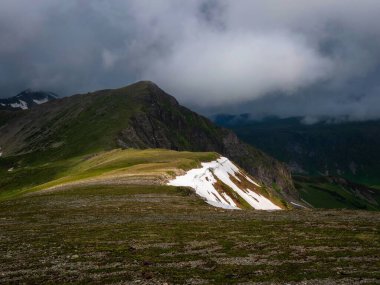 Stony Mountain Ridge 'deki kar tarlası. Dağların eteklerinde kar sürükleniyor, Terektinsky tepesinin yaz manzarası. Altai. Duvar ve ekran için mükemmel yaz resmi.