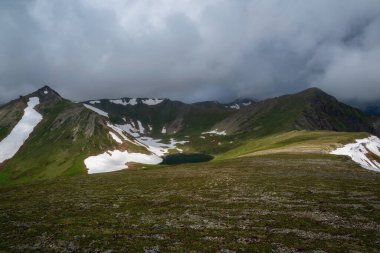 Vadide sıradışı dağ gölü olan dramatik alp manzarası. Güneşli, bulutlu dağ manzaralı. Atmosferik yüksek dağlarda, kara bulutlu gökyüzünün altında yeni yağmış kar. Altai..