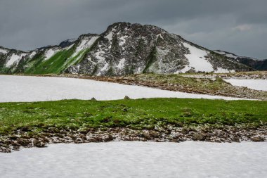 Yazın sert dağlar. Yaz dağlarında değişken hava, eriyen karlar ve son dolu. Terektinsky tepesi, Altai. Duvar ve ekran için mükemmel yaz resmi.