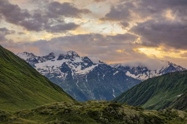 Dağlarda gün batımı. Yüksek rakımlı karlı dağ vadisi olan atmosferik bir manzara. Mor tonlarda gün batımı. Panoramik görünüm.