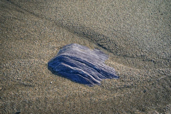 Fluorescent blue slate rock half buried in the sand of a beach in Loiba Espasante Ortigueira Galicia