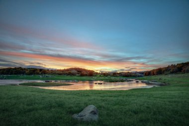 Lugo Galiçya 'daki Minho Nehri boyunca gün batımında yeşil çayırlar ve turuncu bulutlar.