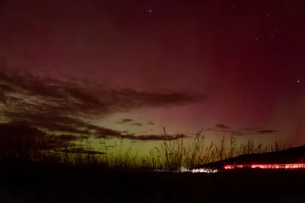 stock image Red and yellow sky glow of Aurora Australis with pink beams over Matakaea (Shag Point) in the South Island of New Zealand. A light trail from car lights indicates the many viewers of this 2024 aurora.