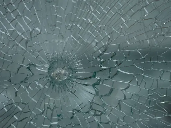 Çatlamış camların radyal desenleri yakın plan görüntüsü. Güvenlik camları çatlıyor ama plastik iç katmanlar parçaları bir arada tutuyor..