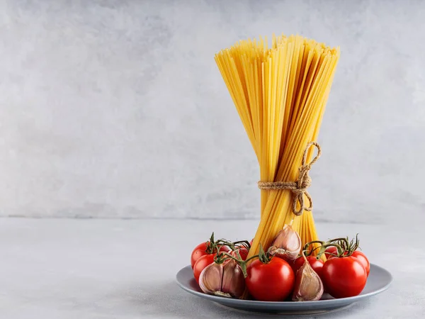トマトとニンニクのスパゲッティパスタを灰色の背景に 灰色の皿の上にイタリアのパスタや野菜を乾燥させます スペースのコピー — ストック写真