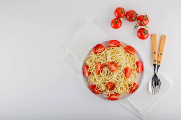 白い背景にチェリートマトとカトラリーとスパゲッティ 白ナプキンにスパゲティパスタと赤トマト 最上階だ スペースのコピー — ストック写真