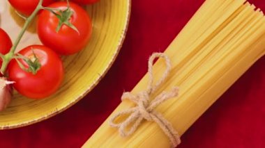 Domatesli siyah ve sarı spagetti ve kırmızı kumaşlı sarımsak. Sarı tabakta taze sebzeler ve sicimle bağlanmış iki demet spagetti. Üst Manzara. El bilgisayarı atışı