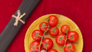 Domatesli siyah ve sarı spagetti ve kırmızı kumaşlı sarımsak. Sarı tabakta taze sebzeler ve sicimle bağlanmış iki demet spagetti. Üst Manzara. El bilgisayarı atışı
