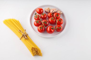 Domatesli spagetti makarna ve beyaz arka planda sarımsak. Balık buğdayından ve sebzeden yapılmış kuru İtalyan makarnası. Üst Manzara. Boşluğu kopyala
