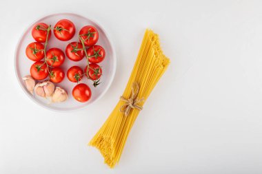 Domatesli spagetti makarna ve beyaz arka planda sarımsak. Balık buğdayından ve sebzeden yapılmış kuru İtalyan makarnası. Üst Manzara. Boşluğu kopyala