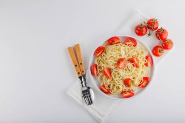 Beyaz arka planda kiraz domatesli spagetti ve çatal bıçak takımı. Makarna ve kırmızı domatesler beyaz peçeteye. Üst Manzara. Boşluğu kopyala