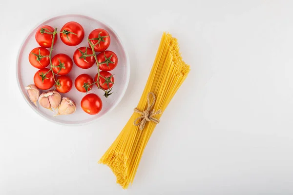 白を背景にトマトとニンニクとスパゲッティパスタ デュラム小麦と野菜から調製ドライイタリアのパスタ 最上階だ スペースのコピー — ストック写真