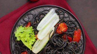 Siyah tabakta sebzeli siyah spagetti. Siyah arka planda mürekkep balığı mürekkebiyle pişirilmiş siyah makarna. Üst Manzara. El bilgisayarı atışı