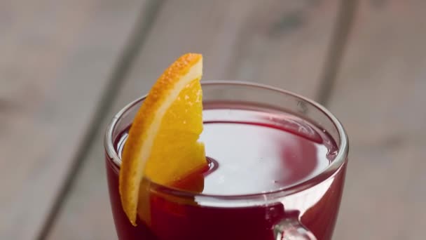 オレンジ色のスライスを持つホットワイングラスは木製のテーブルの上で回転します クリスマスワインはスパイスで飲む 閉じろ — ストック動画