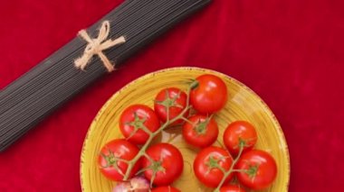 Domatesli siyah ve sarı spagetti ve kırmızı kumaşlı sarımsak. Sarı tabakta taze sebzeler ve sicimle bağlanmış iki demet spagetti. Üst Manzara. El bilgisayarı atışı
