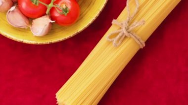 Domatesli siyah ve sarı spagetti ve kırmızı kumaşlı sarımsak. Sarı tabakta taze sebzeler ve sicimle bağlanmış iki demet spagetti. Üst Manzara. El bilgisayarı atışı