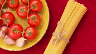 Domatesli siyah ve sarı spagetti ve kırmızı kumaşlı sarımsak. Sarı tabakta taze sebzeler ve sicimle bağlanmış iki demet spagetti. Üst Manzara. El bilgisayarı atışı