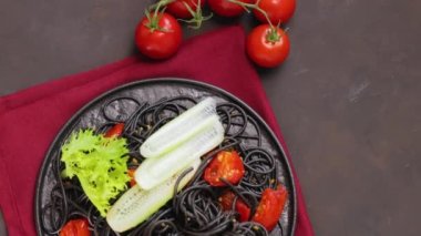 Siyah tabakta sebzeli siyah spagetti. Siyah arka planda mürekkep balığı mürekkebiyle pişirilmiş siyah makarna. Üst Manzara. El bilgisayarı atışı