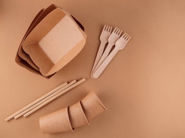 Çevre dostu tek kullanımlık sofra takımı. Kraft kağıt yiyecek kapları, bej arka planda bardaklar ve çatallar. Sıfır atık ve plastiksiz konsept. Boşluğu kopyala