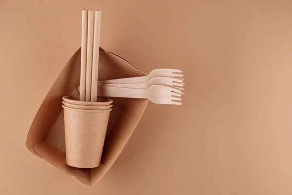Eco-friendly disposable tableware. Kraft paper food containers, cups and forks on beige background. Zero waste and plastic free concept. Copy space