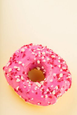 Pembe kremalı ve şekerli çilekli çörek. Sarı arka planda pembe tatlı çörek. Düz yatıyordu. Boşluğu kopyala