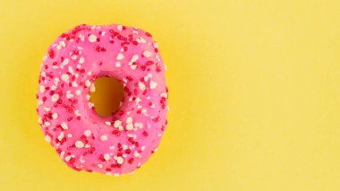 Pembe kremalı ve şekerli çilekli çörek. Sarı arka planda pembe tatlı çörek. Düz yatıyordu. Boşluğu kopyala