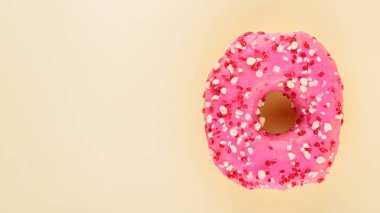 Pembe kremalı ve şekerli çilekli çörek. Sarı arka planda pembe tatlı çörek. Düz yatıyordu. Boşluğu kopyala