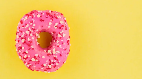 Strawberry donut with pink icing and sprinkles. Sweet pink donut on yellow background. Flat lay. Copy space
