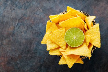 Tortilla chips and lime in a bowl. Nachos chips on a dark background. Top view. Copy space