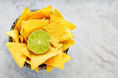 Nachos tortilla chips in a bowl. Bowl of corn tortilla chips and lime on concrete. Top view. Copy space