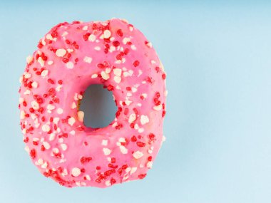 Donut with icing on pastel blue background. Pink donut with colorful toppings. Top view. Copy space