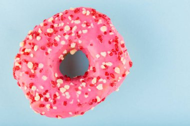 Donut with icing on pastel blue background. Pink donut with colorful toppings. Top view. Copy space