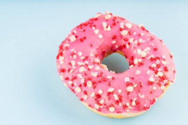 Donut with icing on pastel blue background. Pink donut with colorful toppings. Top view. Copy space