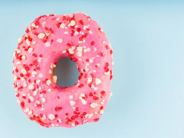 Donut with icing on pastel blue background. Pink donut with colorful toppings. Top view. Copy space