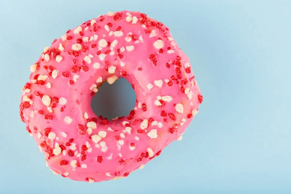 Donut with icing on pastel blue background. Pink donut with colorful toppings. Top view. Copy space