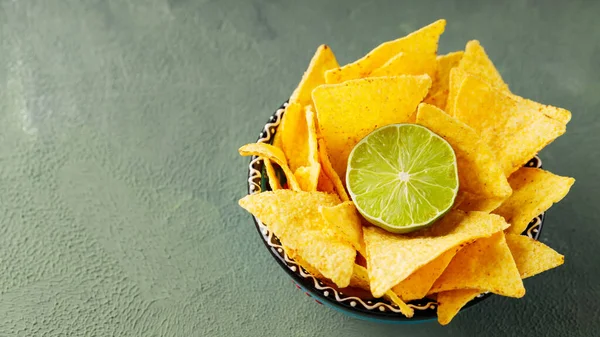 Tortilla chips and lime on a green background. Bowl of crispy nacho chips. Copy space