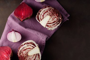 Purple vegetables on a linen napkin. Red beetroot, red onion and radicchio salad on a dark background. Healthy vegan food concept. Top view