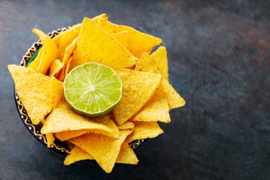 Tortilla chips and lime in a bowl. Nachos chips on a dark background. Top view. Copy space