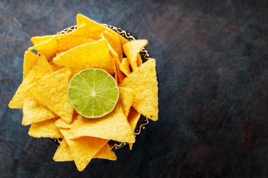 Tortilla chips and lime in a bowl. Nachos chips on a dark background. Top view. Copy space