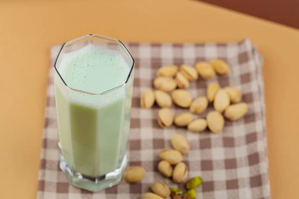 Plant-based natural pistachio milk on a beige background. Tall glass with pistachio milk on a linen napkin. Copy space