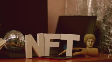 Tasarımcının işyerinde NFT yazıları ve yapay el. Parası ödenmeyen, neon ışıklı harfler. Gelecekçi kripto para birimi konsepti. Dönen kamera görüntüsü